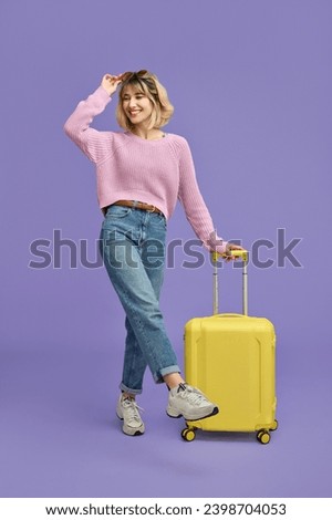 Happy young woman traveler, smiling girl tourist wearing sunglasses with yellow travel suitcase ready for summer vacation trip looking aside standing isolated on purple background. Full body vertical.