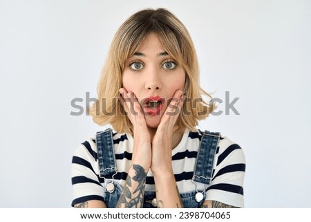 Shocked pretty gen z blonde young woman, surprised 20s girl with short blond hair and tattoos looking at camera feeling amazed or excited emotion isolated on white background. Close up face portrait.
