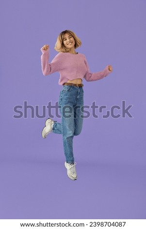 Joyful generation z blonde girl dancing jumping isolated on purple background. Happy pretty gen z young woman wearing jeans and pink sweater dancing jumping isolated on purple background. Full body.