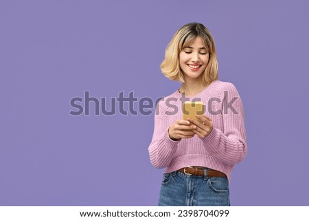 Happy pretty gen z blonde young woman model holding smartphone looking at cell texting message, smiling girl using mobile apps on cell phone standing isolated on purple background with cellphone.