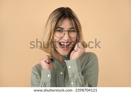 Happy excited gen z blonde young woman, glad college student girl with short blond hair wearing glasses celebrating winning prize, admission with yes gesture standing isolated on beige background. Royalty-Free Stock Photo #2398704121