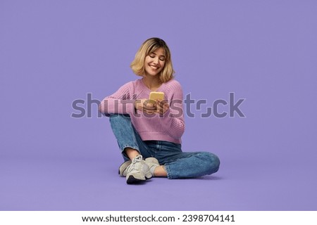 Happy pretty gen z blonde young woman model holding smartphone looking at cell texting message, smiling girl using mobile apps on cell phone sitting isolated on purple background with cellphone.