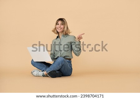Happy gen z blonde young woman with laptop, smiling european student girl with short blond hair using computer elearning online sitting pointing aside at copy space isolated on beige background.