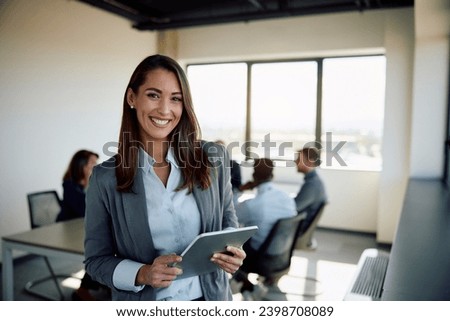 Young happy businesswoman using digital tablet in meeting room and looking at camera. Copy space. Royalty-Free Stock Photo #2398708089