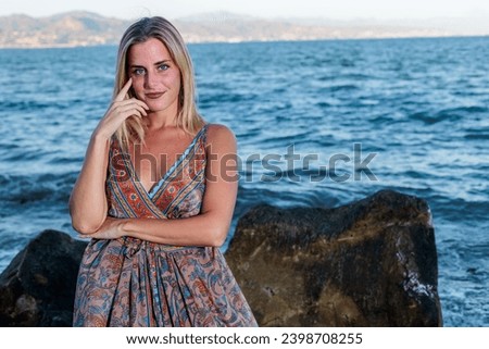 very pretty blonde woman in dress posing on the beach with the sea in the background