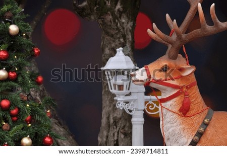 Reindeer with decorated Christmas tree and dark background with blurred lights