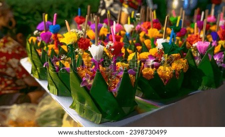 A photo of several bright green banana leaf krathongs with petals carefully arranged on a clean white future board. Inside the krathong are bright yellow marigolds, purple orchids, artificial flowers