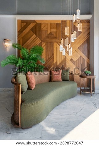 Stylish green couch in a modern living room, with a background of a warm decorated wood cladding wall and modern chandelier hanging from the ceiling