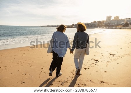 Rear view of couple in love is walk holding hands across the sunny beach. High quality photo