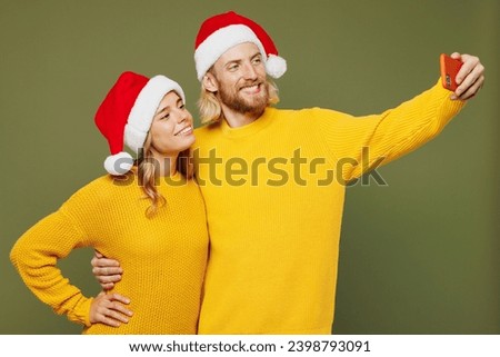 Merry young couple two friends man woman wear sweater Santa hat posing doing selfie shot on mobile cell phone isolated on plain green background. Happy New Year celebration Christmas holiday concept