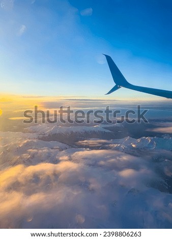 view of the mountains from the height of a flying airplane, clouds, mountains, airplane wing, blue sky, dawn.