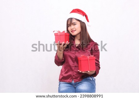 Photo portrait of beautiful young asian girl carrying gift box in christmas santa claus hat modern shiny red shirt outfit hands raise box up and down on white background for promotion and advertising