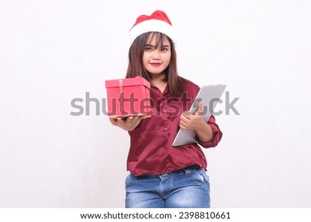 Beautiful young Southeast Asian woman smiling giving 3 gift boxes hamper and tablet laptop at Christmas wearing santa hat modern red shirt outfit white background for promotion and advertising