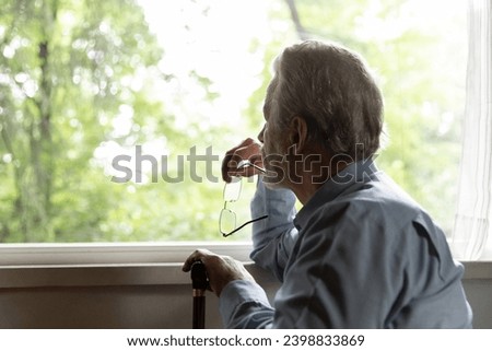 Retirement problem. Pensive old man nursing home patient sit by window hold glasses walking stick lost in sad thoughts. Upset aged male think about bad health loneliness miss deceased wife. Copy space Royalty-Free Stock Photo #2398833869