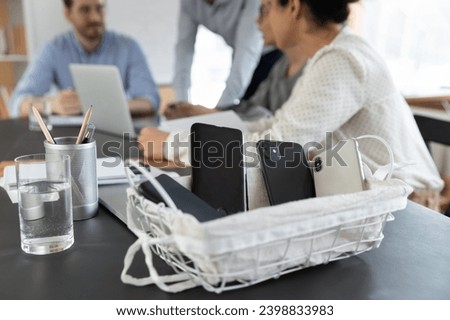 Close up of modern smartphones in box during businesspeople brainstorm cooperate at office meeting. Cellphones put away in basket, no cell gadgets allowed during employees briefing at workplace. Royalty-Free Stock Photo #2398833983
