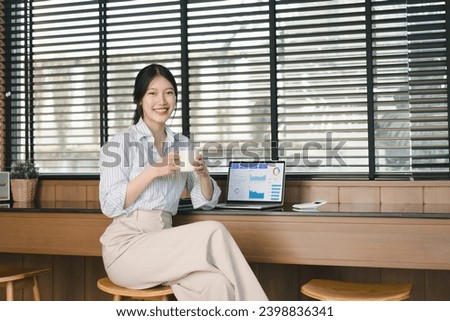 Portrait of young Asian businesswoman smiling and holding a cup of coffee indoors