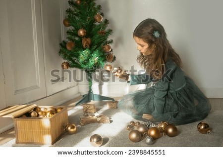 Little girl in beautiful green dress decorates Christmas tree with golden balls.