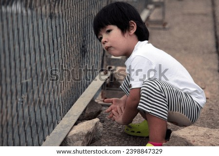 Exterior photo view of a 3 years old handsome good looking male curious baby boy looking around as he is adventurous looking at somethings that interest him behind a fence during a family  day out