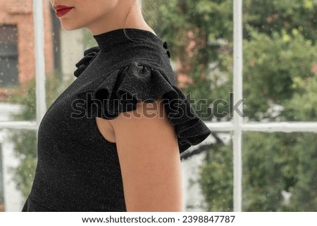 Detail photo of caucasian woman wearing a black dress with shoulder detail. no face, beautiful light space, window and green trees.