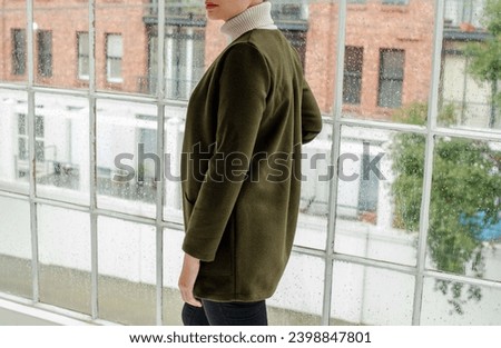 Photo of caucasian woman wearing a green long jacket, no face, beautiful light space, window.