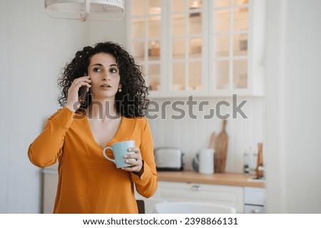 Surprised woman talking phone at home with puzzled face expression received breathtaking news, crisis, failure. Housewife at kitchen, Royalty-Free Stock Photo #2398866131