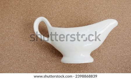 Close up photo of a cute white ceramic barbecue sauceboat with handle  on  a brown background. Royalty-Free Stock Photo #2398868839