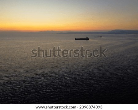 A photorealistic image of a sunset over the ocean with two ships on the horizon. The sky is orange and yellow, with the sun setting on the horizon. The ocean is dark blue and calm.
