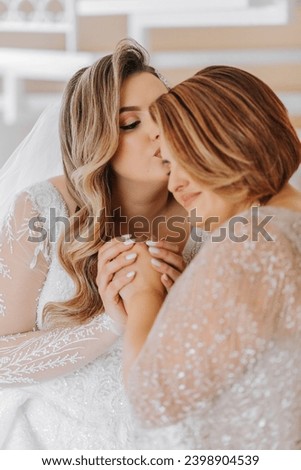 A beautiful and happy mother and her daughter, the bride, are standing next to each other. The best day for parents. Tender moments at the wedding. Royalty-Free Stock Photo #2398904539