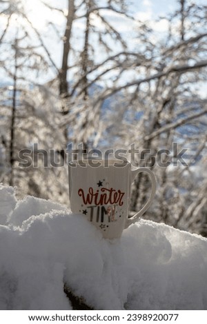 A mug of hot tea on a snowy branch under the winter sun