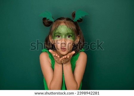 An attractive girl with a dragon scale pattern on her face, on a green studio background, sends an air kiss