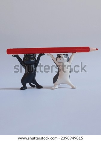 Funny toy dancing kittens and a red pen on a light background. A humorous business training concept. Concept of the effectiveness of teamwork and leadership in the working group. Daylight