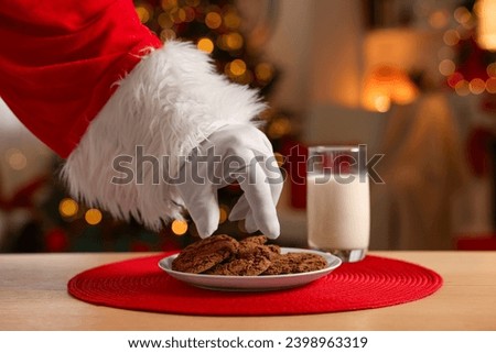 Merry Christmas. Santa Claus taking cookies from plate on table in room, closeup