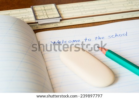 Welcome to the school, an exercise book and pencil with eraser and slide rule on the wooden table