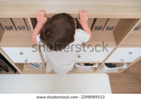 Baby climbs onto a cabinet, dangers at home with risk of injury. Kid aged two (two year old)