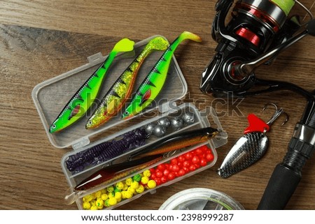 Fishing rod with spinning reel and baits on wooden background, flat lay Royalty-Free Stock Photo #2398999287
