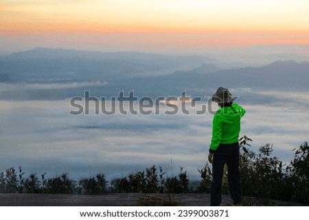 A male tourist takes a photo of the morning white mist view at Pha Nok Aen. Phu Kradueng National Park in Loei Province,Thailand.