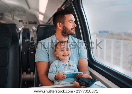 The adorable baby watches cartoons and giggles, while dad rests and enjoys the view while they ride the train
