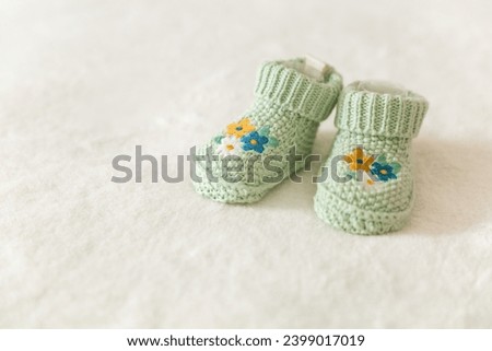 Green knitted baby socks with embroidery, handmade knitted booties on a white background with copy space. Pregnancy and motherhood concept, first birthday banner, handmade socks, baby warm clothes. Royalty-Free Stock Photo #2399017019