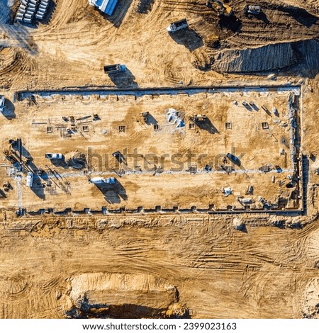 This high-resolution image captures the early morning activity at a construction site from a bird's-eye view. The golden sunlight casts long shadows, highlighting the busy workers, machinery.