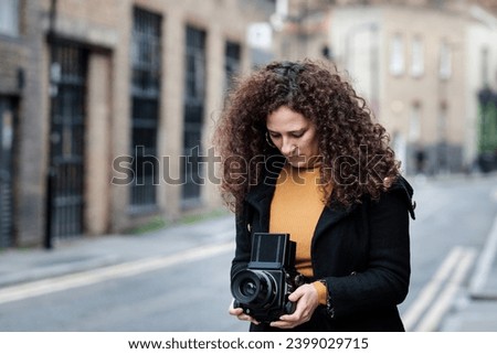 Mature female photographer is using medium format analog film camera in a London street. Classic hobbies to technology involved concept.