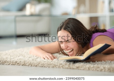 Happy woman lying on the floor laughing hilariously reading a book at home Royalty-Free Stock Photo #2399040075