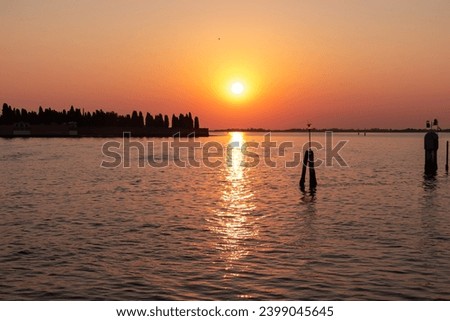 Scenic sunset view on San Michele island at Venetian lagoon in Venice, Veneto, Northern Italy, Europe. Reflection in the water creating romantic atmosphere. Orange red sky. Silhouette of landmarks Royalty-Free Stock Photo #2399045645