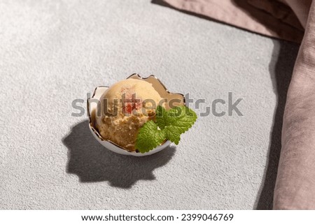 A ball of peach ice cream with a mint leaf in a beautiful creamer
