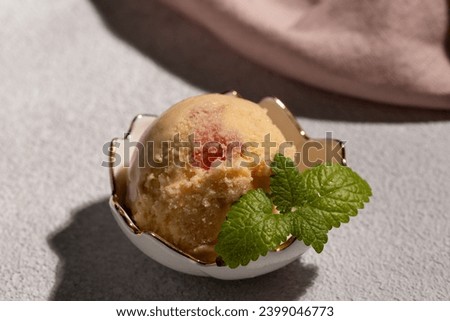 A ball of peach ice cream with a mint leaf in a beautiful creamer