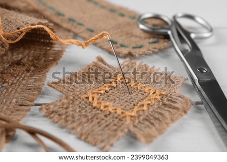 Pieces of burlap fabric with stitches, needle and scissors on white wooden table, closeup