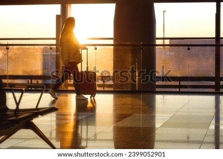 An airport passenger with a suitcase walks against the backdrop of the morning sun. View from the airport to the sun through the glass.