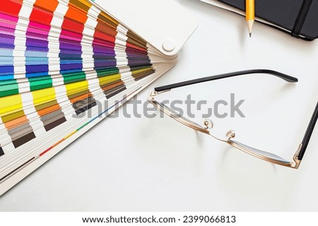 Paint swatches color guide, sketchbook and glasses on white table, top view. Designer workplace