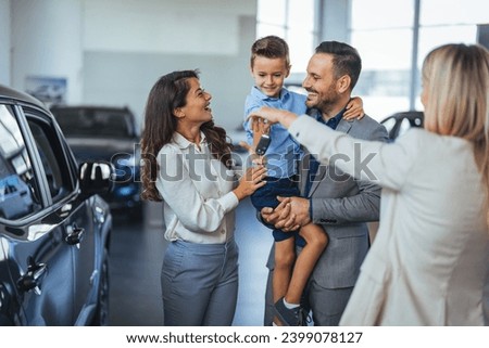 Young happy family enjoying while buying a new car in a showroom. Saleswoman at car dealership center helping family to choose new family vehicle. Family in a car dealership 