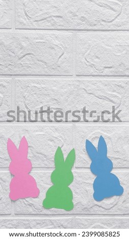 Paper decoration in shape rabbits. Vertical photo. Place for text. Colored bunnies on background of white brick wall. Copy space. Flat lay. Template for website, articles, advert for preschool, school