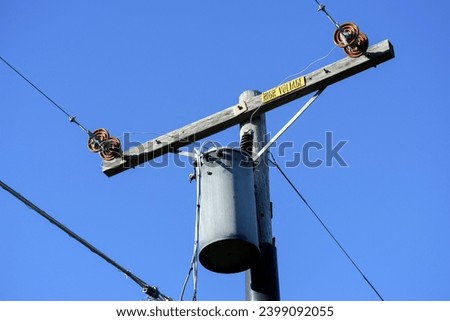 Single phase distribution transformer on the weathered wooden pole. Yellow high voltage sign.
